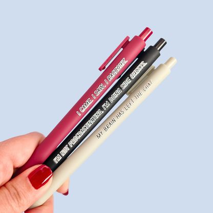 Three pens with humorous text held by a hand against a light blue background
