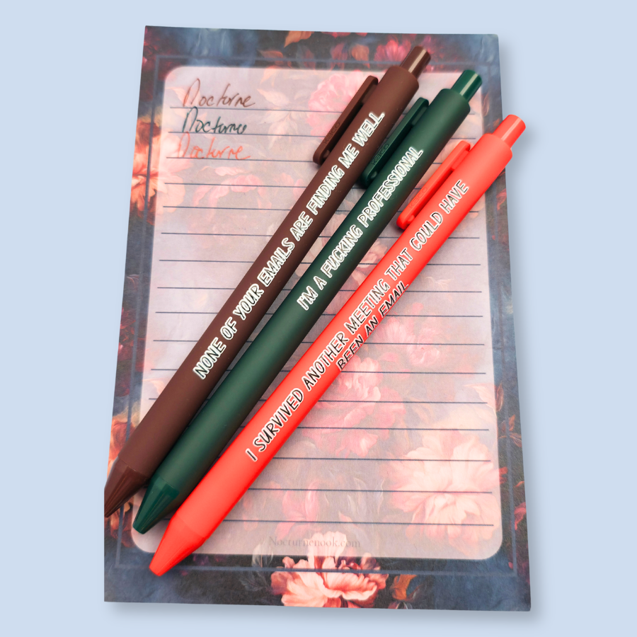 Three pens with quotes. "None of your emails are finding me well" on a brown pen, " I'm a fucking professional" on a forest green pen, and "I survived another meeting that could have been an email" on a orange pen.