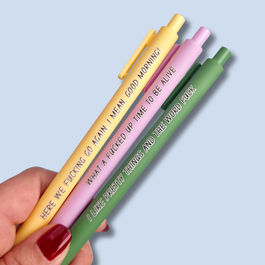 Three pens with sayings on them. "here we fucking go again. I mean, Good morning!"(yellow pen), "What a fucked up time to be alive" (lilac pen), "I like pretty things and the word fuck" ( moss green pen)