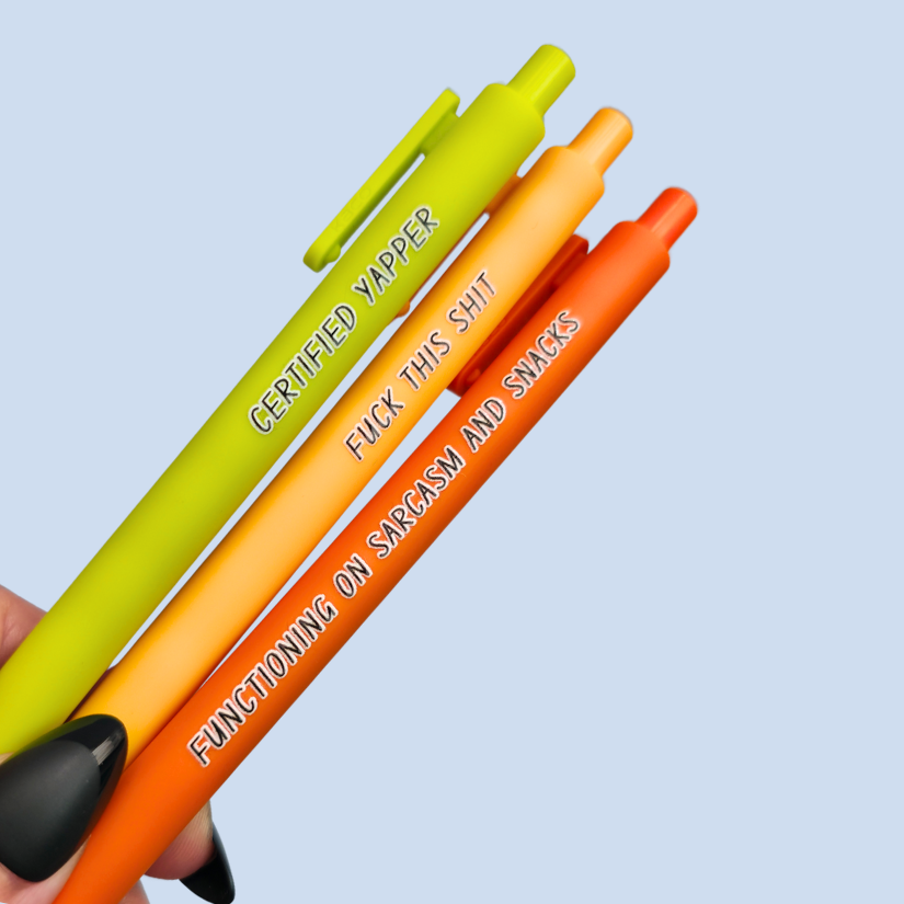 Three pens with sayings on them. "certified yapper" (lime green pen), "Functioning on sarcasm and snacks" (neon orange pen), "fuck this shit" (sunflower yellow pen).