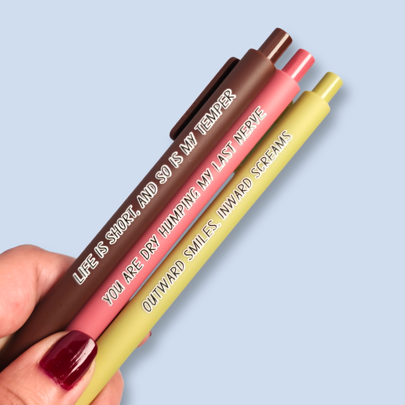 Three pens with humorous text on a light blue background. Text reads, "Life is short, and so is my temper" on a brown pen, "You are dry humping my last nerve" on a pink pen and "Outward smiles, inward screams" on a olive green pen