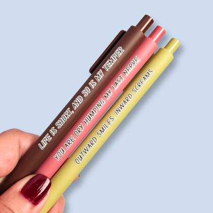 Three pens with humorous text on a light blue background. Text reads, "Life is short, and so is my temper" on a brown pen, "You are dry humping my last nerve" on a pink pen and "Outward smiles, inward screams" on a olive green pen