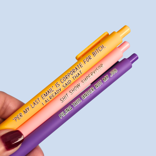 Three pens with sayings on them. "Per My Last Email" is Corporate for bitch, I already said that."(bright yellow pen), "Shit show supervisor" (pastel Pink pen), "Filing this under not my job" ( purple pen).