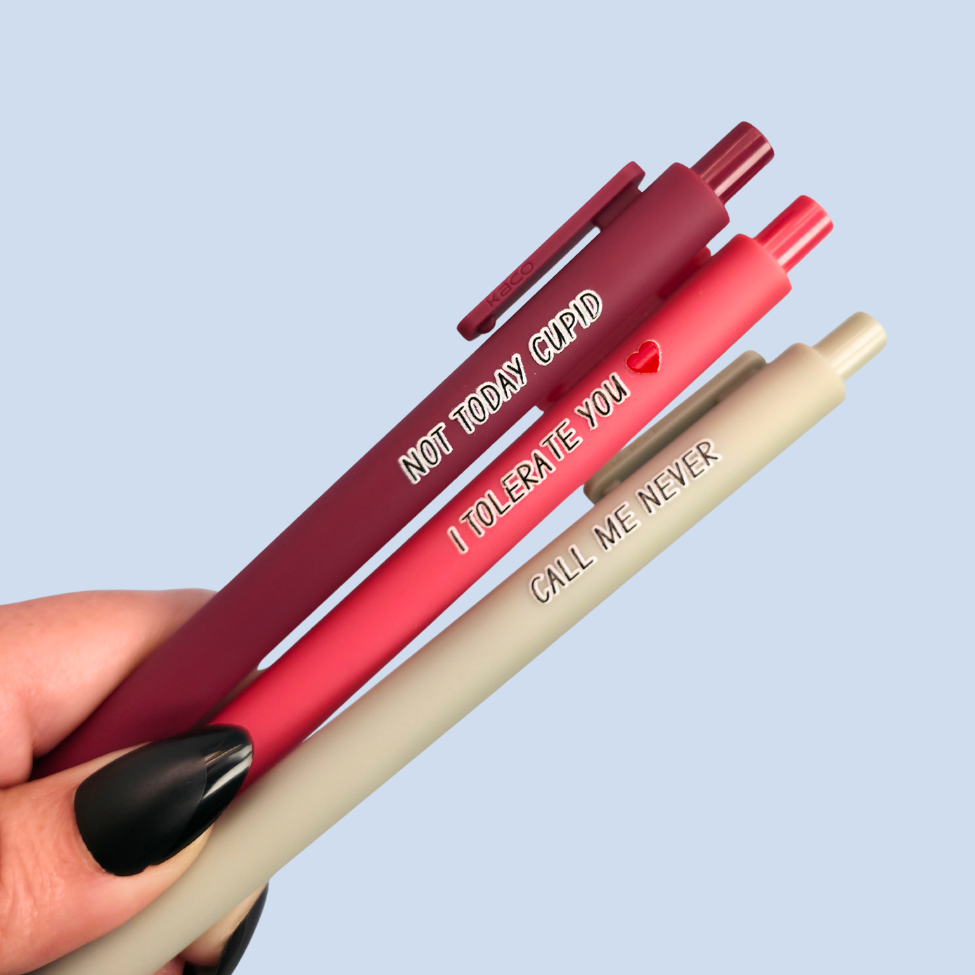 Three pens with humorous text held by a hand against a light blue background