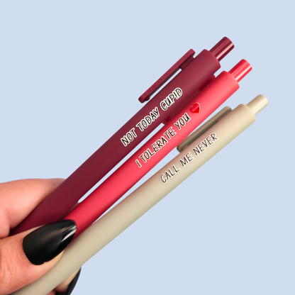 Three pens with humorous text held by a hand against a light blue background