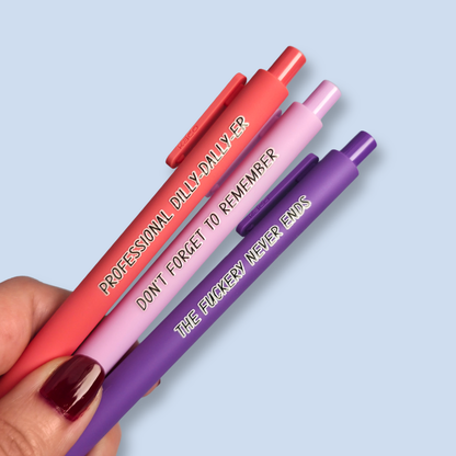 Three pens with humorous text on a light blue background. Text reads, "Professional Dilly-Dally-Er" on a Salmon pink pen, "Don't forget to remember" on a lilac pen and "The fuckery never ends" on a purple pen