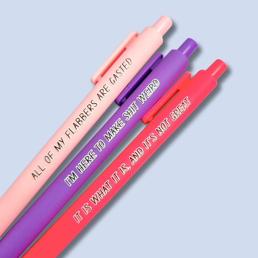 Three pens with sayings on them. "All of my flabbers are gasted" (pastel pink pen), "I'm here to make shit weird" (purple pen), "It Is what it is, and it's not great" ( neon pink pen).