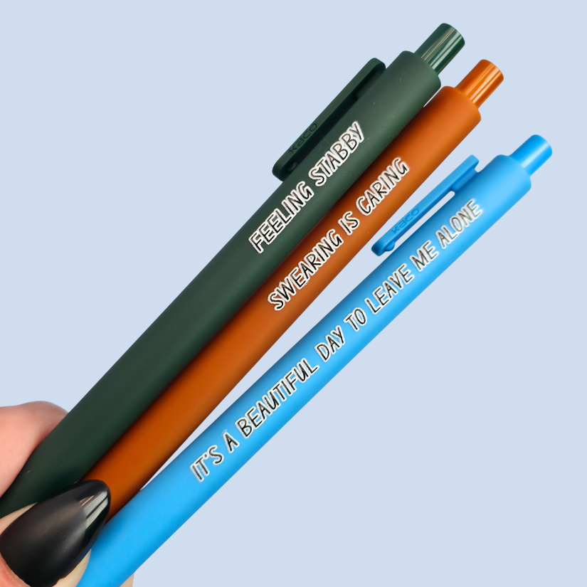 Three pens with sayings on them. "Feeling Stabby."(forest green pen), "It's a beautiful day to leave me alone" (bright blue pen), "Swearing is caring" ( sienna pen).