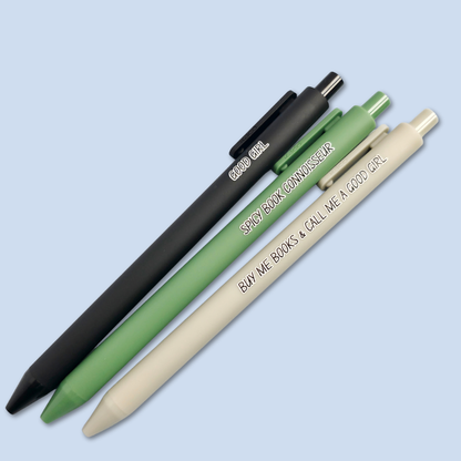 Three pens with quotes. "Good Girl" on a Black pen, "Spicy Book Connoisseur" on a green pen, and "Buy me books and call me a good girl" on a grey pen.