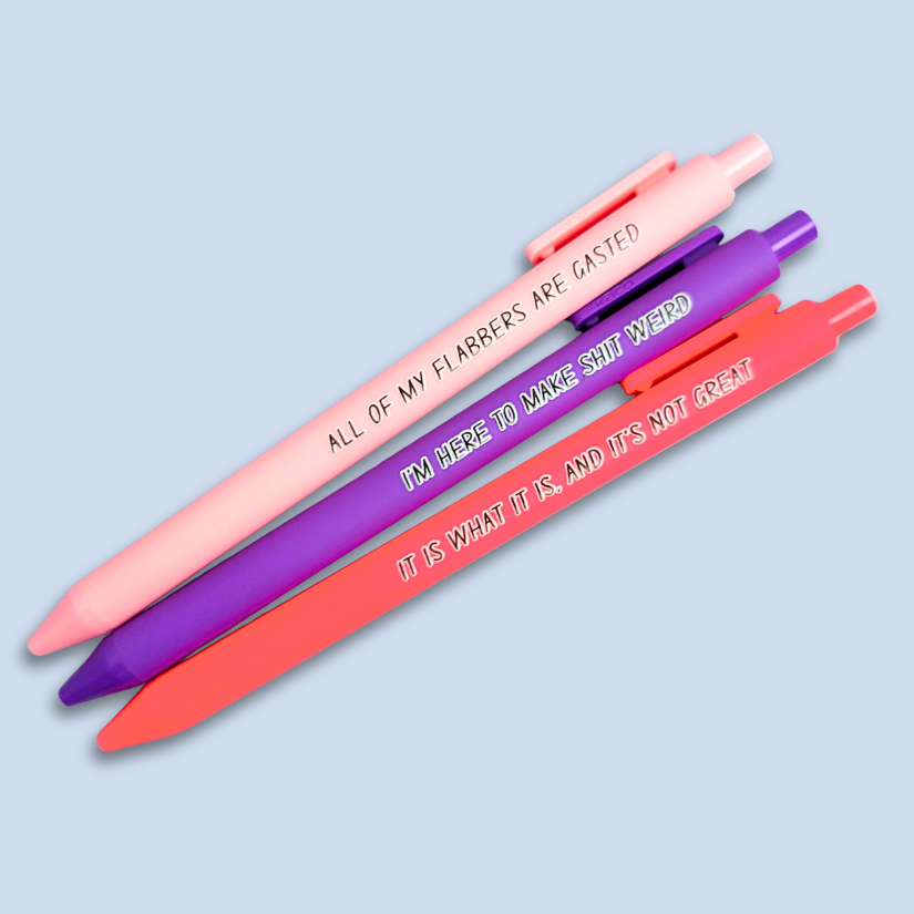 Three pens with sayings on them. "All of my flabbers are gasted" (pastel pink pen), "I'm here to make shit weird" (purple pen), "It Is what it is, and it's not great" ( neon pink pen).