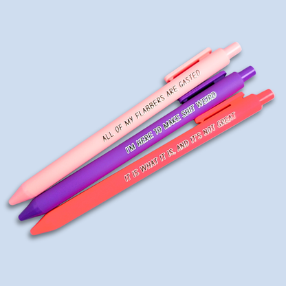 Three pens with sayings on them. "All of my flabbers are gasted" (pastel pink pen), "I'm here to make shit weird" (purple pen), "It Is what it is, and it's not great" ( neon pink pen).