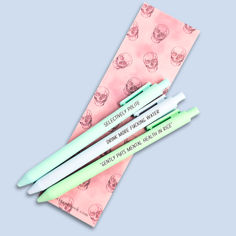 Three pens with humorous text on a light blue background. Text reads, "Gently puts mental health in rice" on a pastel green pen, "Selectively polite" on a mint pen and "drink more fucking water" on a pastel blue pen
