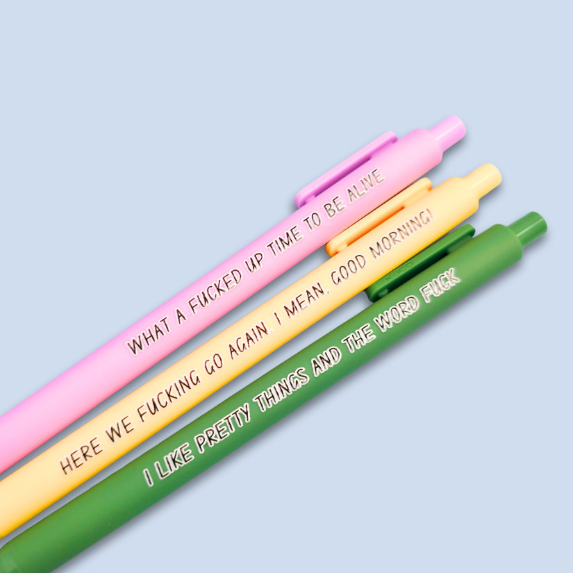 Three pens with sayings on them. "here we fucking go again. I mean, Good morning!"(yellow pen), "What a fucked up time to be alive" (lilac pen), "I like pretty things and the word fuck" ( moss green pen)