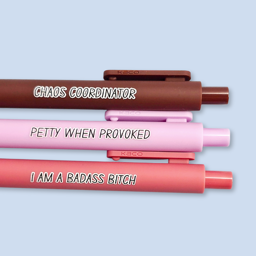 Three pens with humorous text. "Petty when provoked" on a lilac pen, "chaos coordinator" on a brown pen, and "I am a badass bitch" on a pink pen