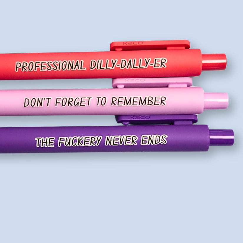 Three pens with humorous text on a light blue background. Text reads, "Professional Dilly-Dally-Er" on a Salmon pink pen, "Don't forget to remember" on a lilac pen and "The fuckery never ends" on a purple pen