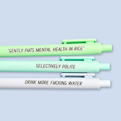 Three pens with humorous text on a light blue background. Text reads, "Gently puts mental health in rice" on a pastel green pen, "Selectively polite" on a mint pen and "drink more fucking water" on a pastel blue pen