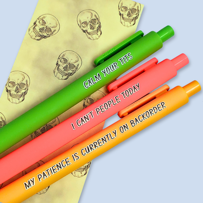 Three colorful pens with humorous text on a light blue background over a yellow bookmark with skull designs.