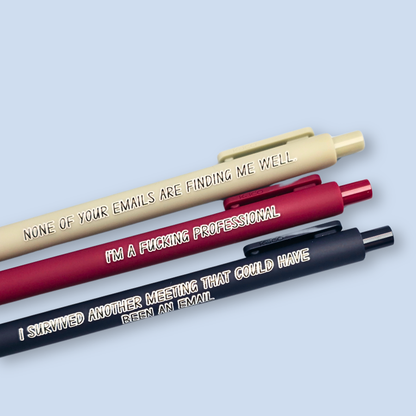 Three pens with quotes. "None of your emails are finding me well" on a grey pen, " I'm a fucking professional" on a dark red pen, and "I survived another meeting that could have been an email" on a navy blue pen.