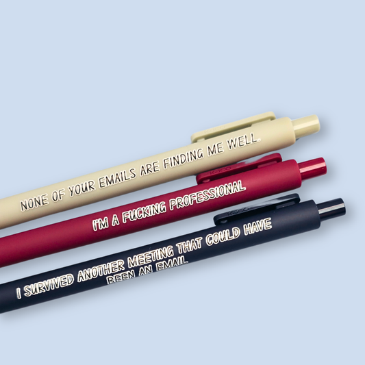 Three pens with quotes. "None of your emails are finding me well" on a grey pen, " I'm a fucking professional" on a dark red pen, and "I survived another meeting that could have been an email" on a navy blue pen.
