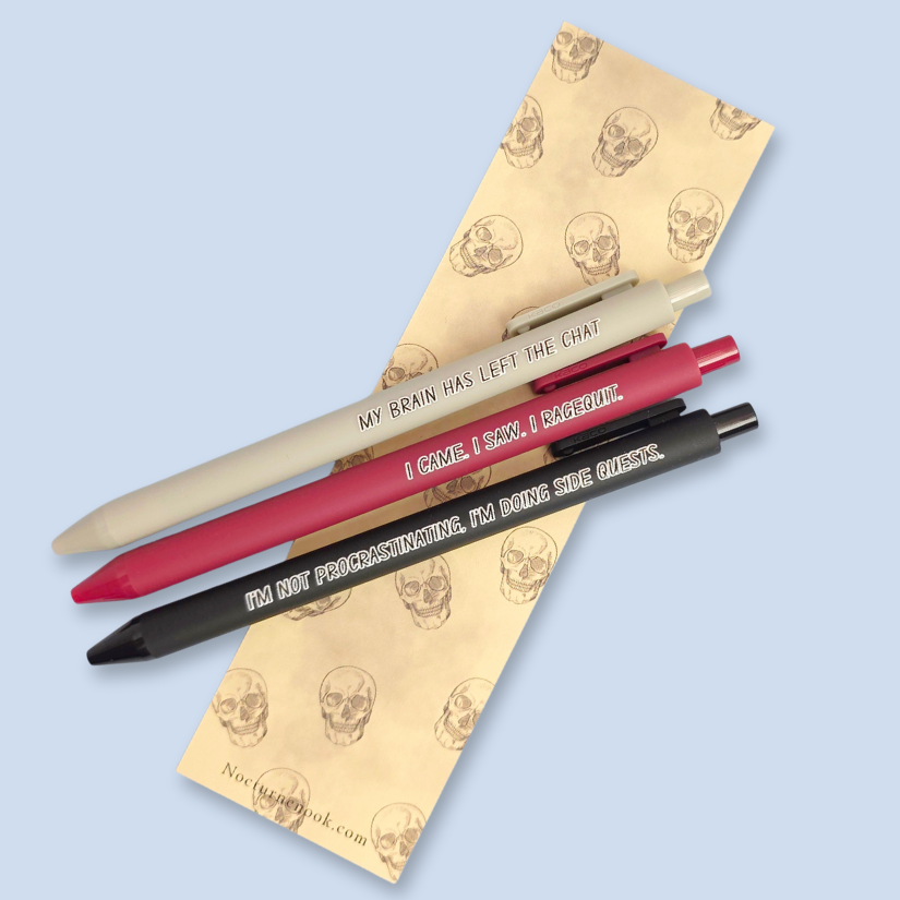 Three pens with humorous text on a yellow bookmark with skull designs.