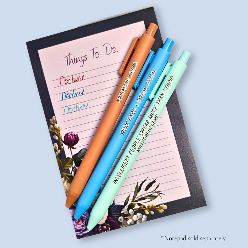 Three pens with sayings on them. "Swearing Helps"(Caramel  pen), "Work Hard & Swear often" (bright blue pen), "Intelligent people swear more than stupid motherfuckers" ( mint pen). They are on top of a notepad, with a sample of the ink. Ink matches the color of the pen. Notepad not included