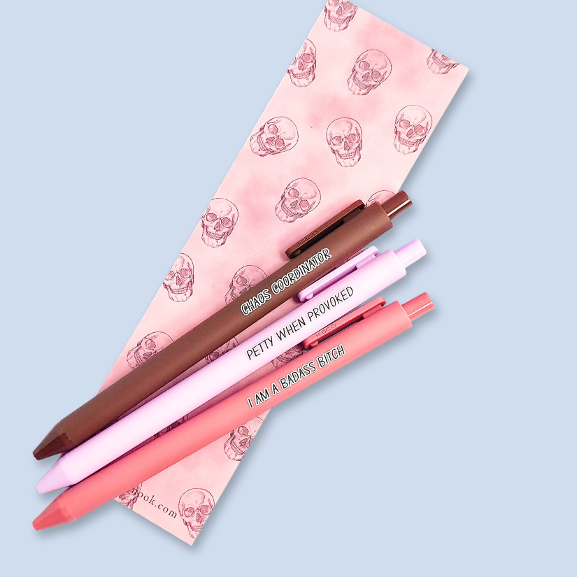 Three pens with humorous text. "Petty when provoked" on a lilac pen, "chaos coordinator" on a brown pen, and "I am a badass bitch" on a pink pen
