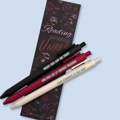 Three pens with sayings on them. "Dark romance is the vibe" (light grey pen), "You had me at trigger warning" (wine pen), "Touch her and die vibes" ( black pen).