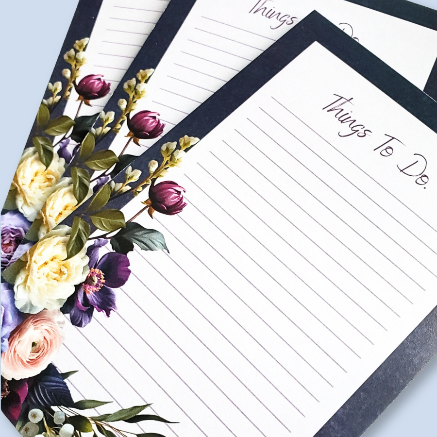 A vertical lined notepad with the heading 'Things To Do.' at the top, framed by a black border and decorated with purple, cream, and pink flowers along the lower left corner, shown on a light blue background.