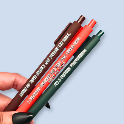 Three pens with quotes. "None of your emails are finding me well" on a brown pen, " I'm a fucking professional" on a forest green pen, and "I survived another meeting that could have been an email" on a orange pen.