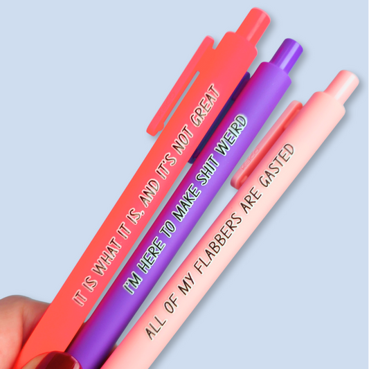 Three pens with sayings on them. "All of my flabbers are gasted" (pastel pink pen), "I'm here to make shit weird" (purple pen), "It Is what it is, and it's not great" ( neon pink pen).