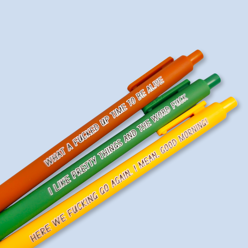 Three pens with sayings on them. "here we fucking go again. I mean, Good morning!"(bright yellow pen), "What a fucked up time to be alive" (sienna pen), "I like pretty things and the word fuck" ( green pen)