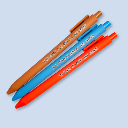 Three pens with sayings on them. "All of my flabbers are gasted" (bright blue pen), "I'm here to make shit weird" (neon orange pen), "It Is what it is, and it's not great" ( caramel pen).