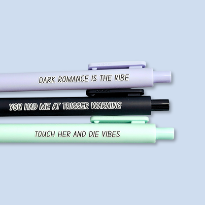 Three pens with sayings on them. "Dark romance is the vibe" (lavender pen), "You had me at trigger warning" (black pen), "Touch her and die vibes" ( mint pen).