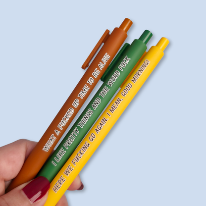 Three pens with sayings on them. "here we fucking go again. I mean, Good morning!"(bright yellow pen), "What a fucked up time to be alive" (sienna pen), "I like pretty things and the word fuck" ( green pen)
