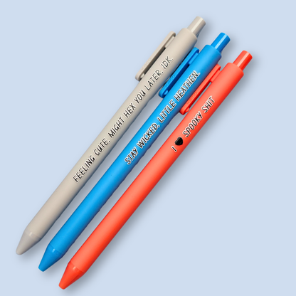Three pens with humorous text on a light blue background. Text reads, "Feeling cute, might hex you later, IDK" on a light grey pen, "Stay wicked, little heathen" on a bright blue pen and "I  heart spooky shit" on a orange pen