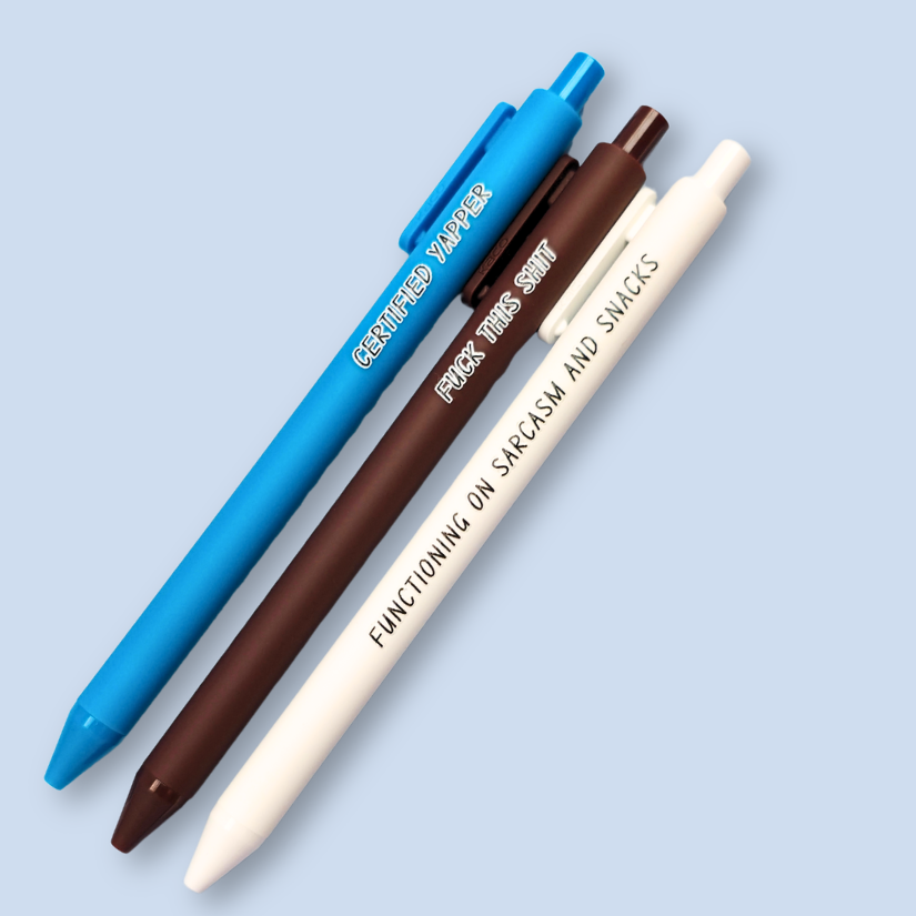 Three pens with sayings on them. "certified yapper" (bright blue pen), "Functioning on sarcasm and snacks" (white pen), "fuck this shit" (brown pen).