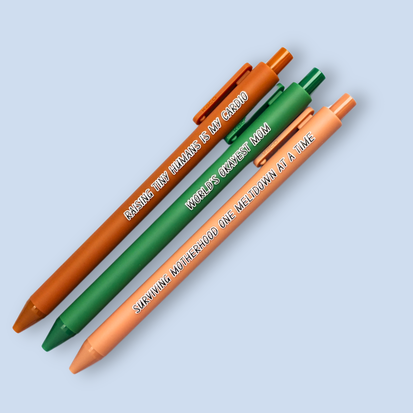Three pens with humorous text on a light blue background. Text reads, "Raising tiny humans is my cardio" on a sienna pen, "World's okayest mom" on a green pen and "surviving motherhood one meltdown at a time" on a caramel pen
