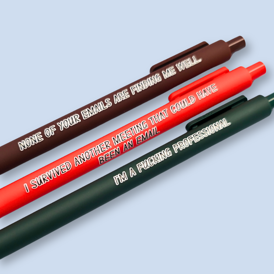 Three pens with quotes. "None of your emails are finding me well" on a brown pen, " I'm a fucking professional" on a forest green pen, and "I survived another meeting that could have been an email" on a orange pen.