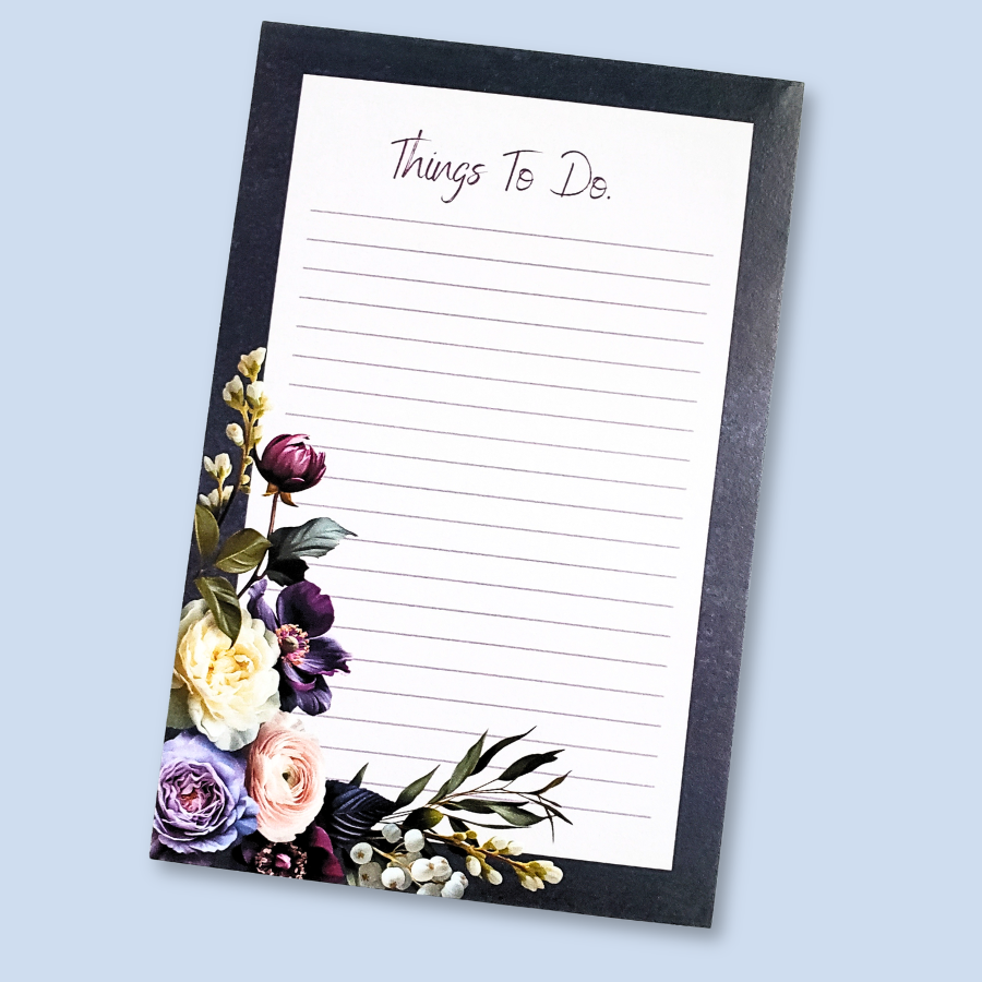 A vertical lined notepad with the heading 'Things To Do.' at the top, framed by a black border and decorated with purple, cream, and pink flowers along the lower left corner, shown on a light blue background.