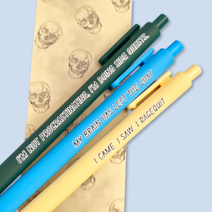 Three pens with humorous text on a skull-patterned bookmark