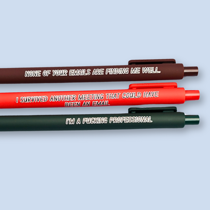 Three pens with quotes. "None of your emails are finding me well" on a brown pen, " I'm a fucking professional" on a forest green pen, and "I survived another meeting that could have been an email" on a orange pen.