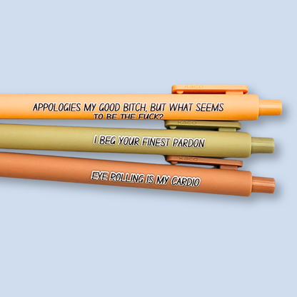 Three novelty gel pens in orange, olive green, and terracotta pink, stacked horizontally on a light blue background. Each pen features bold black text with a humorous statement.