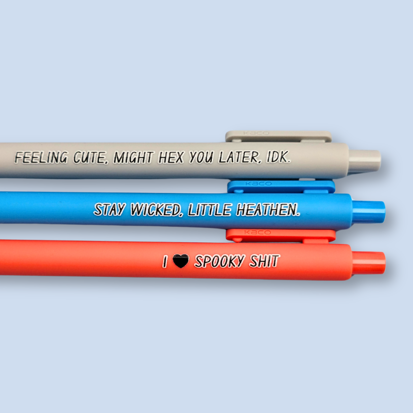Three pens with humorous text on a light blue background. Text reads, "Feeling cute, might hex you later, IDK" on a light grey pen, "Stay wicked, little heathen" on a bright blue pen and "I  heart spooky shit" on a orange pen