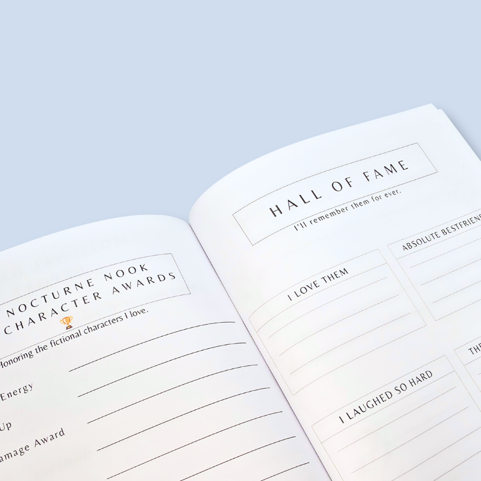 An open book or planner spread showing printed writing prompts, including 'Hall of Fame' and 'Nocturne Nook Character Awards,' photographed on a pale blue background.