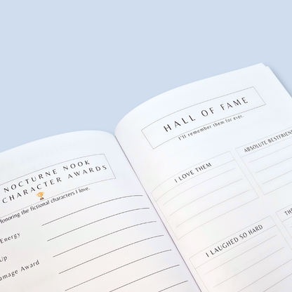 An open book or planner spread showing printed writing prompts, including 'Hall of Fame' and 'Nocturne Nook Character Awards,' photographed on a pale blue background.