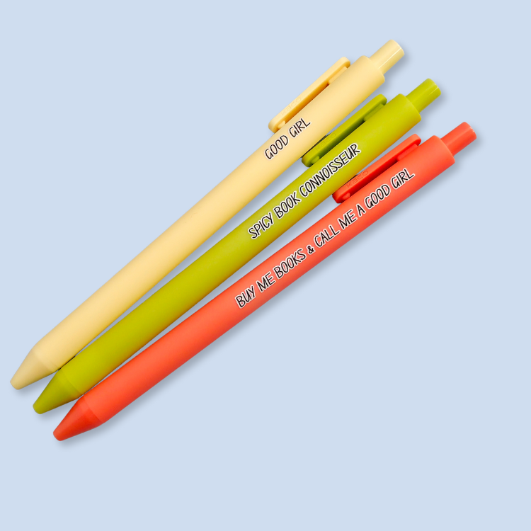 Three pens with quotes. "Good Girl" on a yellow pen, "Spicy Book Connoisseur" on a neon green pen, and "Buy me books and call me a good girl" on a neon orange pen.