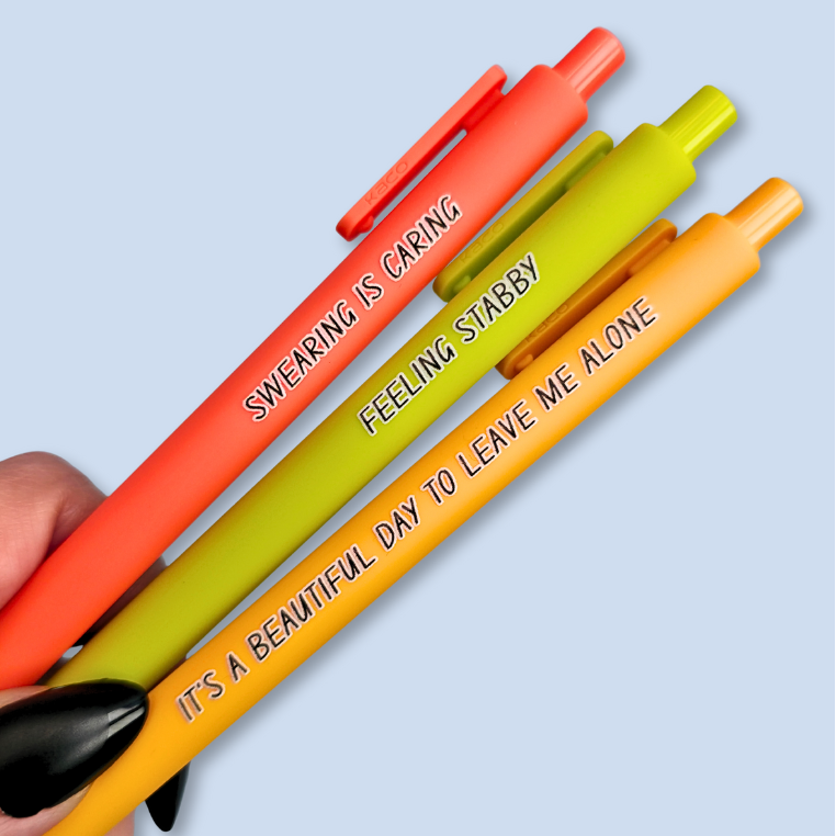 Three pens with sayings on them. "Feeling Stabby."(Lime pen), "It's a beautiful day to leave me alone" (Sunflower yellow pen), "Swearing is caring" ( neon orange pen).