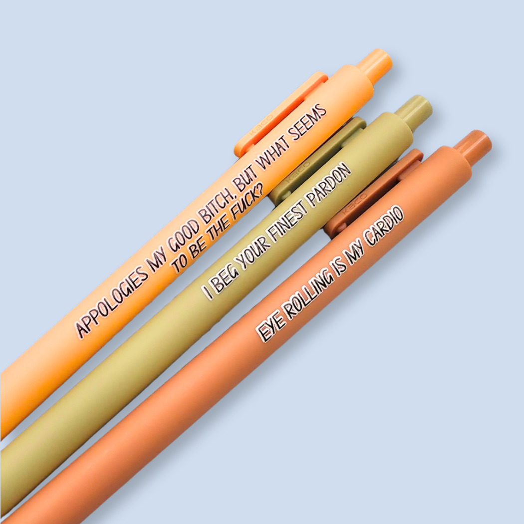 Three retractable gel pens in orange, beige, and peach tones, arranged diagonally on a light blue background. Each pen features black printed text with a humorous phrase.