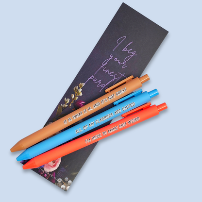 Three pens with sayings on them. "All of my flabbers are gasted" (bright blue pen), "I'm here to make shit weird" (neon orange pen), "It Is what it is, and it's not great" ( caramel pen).