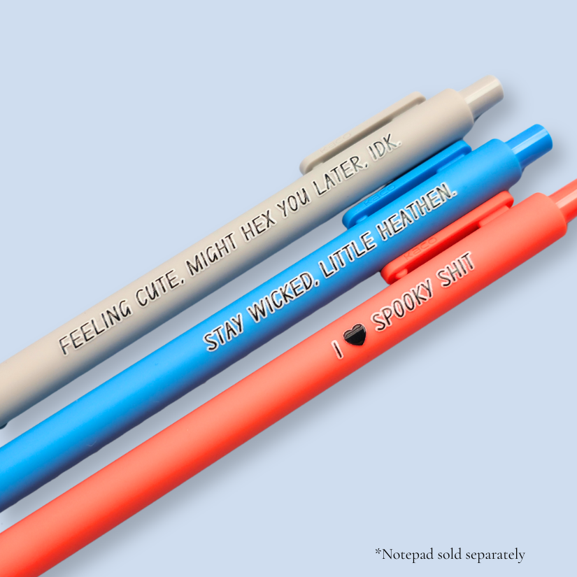 Three pens with humorous text on a light blue background. Text reads, "Feeling cute, might hex you later, IDK" on a light grey pen, "Stay wicked, little heathen" on a bright blue pen and "I  heart spooky shit" on a orange pen